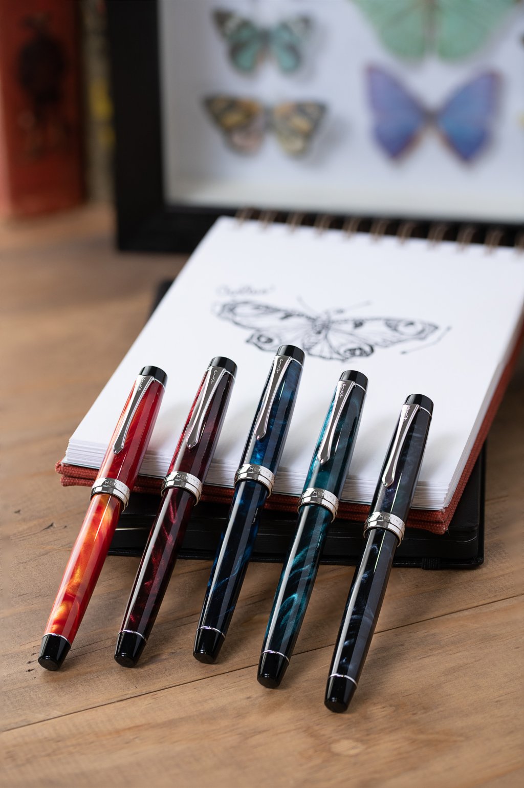 168网澳洲5结果官方PILOT Custom Heritage SE fountain pens in five colours, leaning against a note pad with a butterfly drawing.